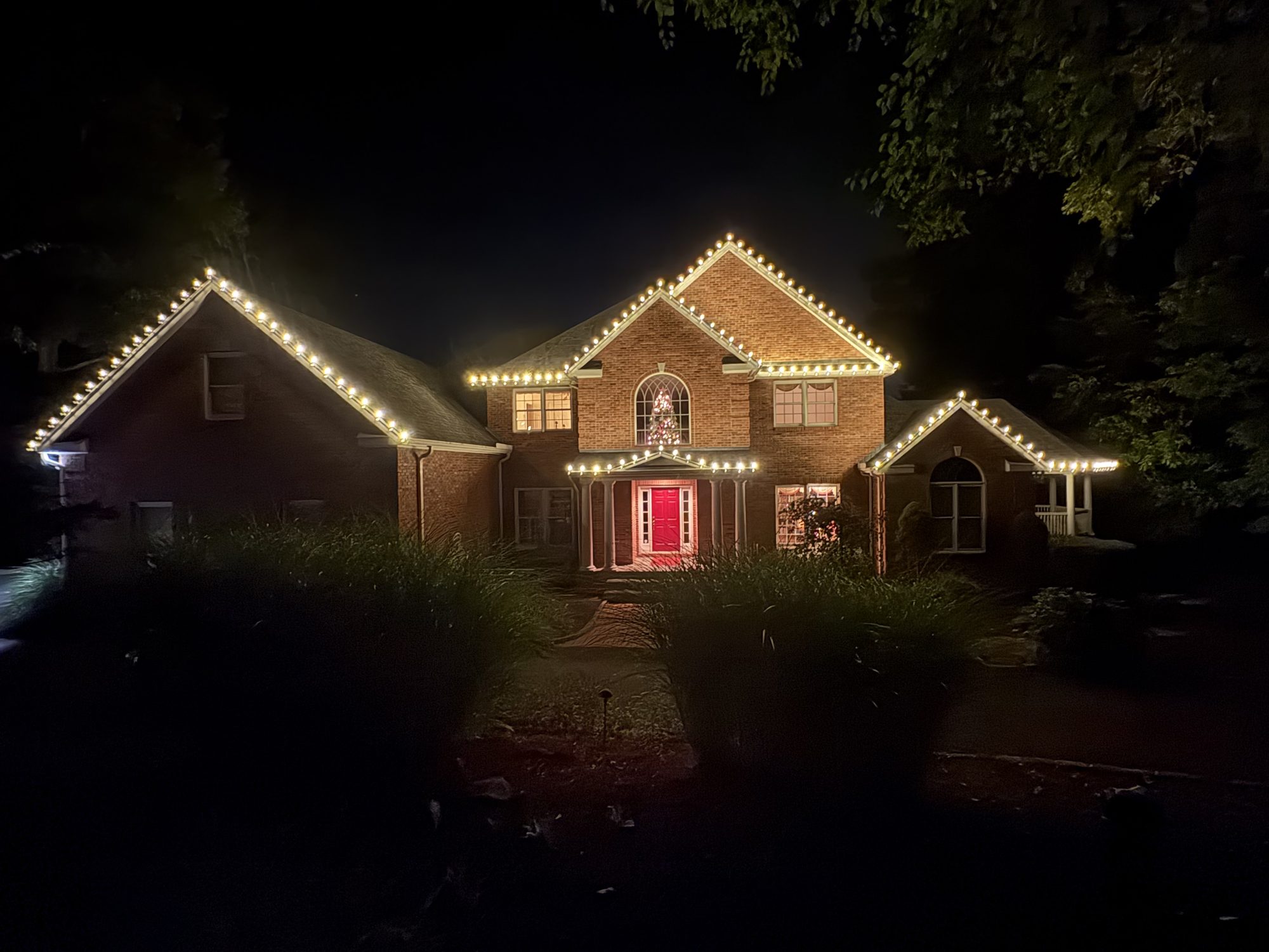 Brick colonial with three peaks and the roofline outlined in warm white lights