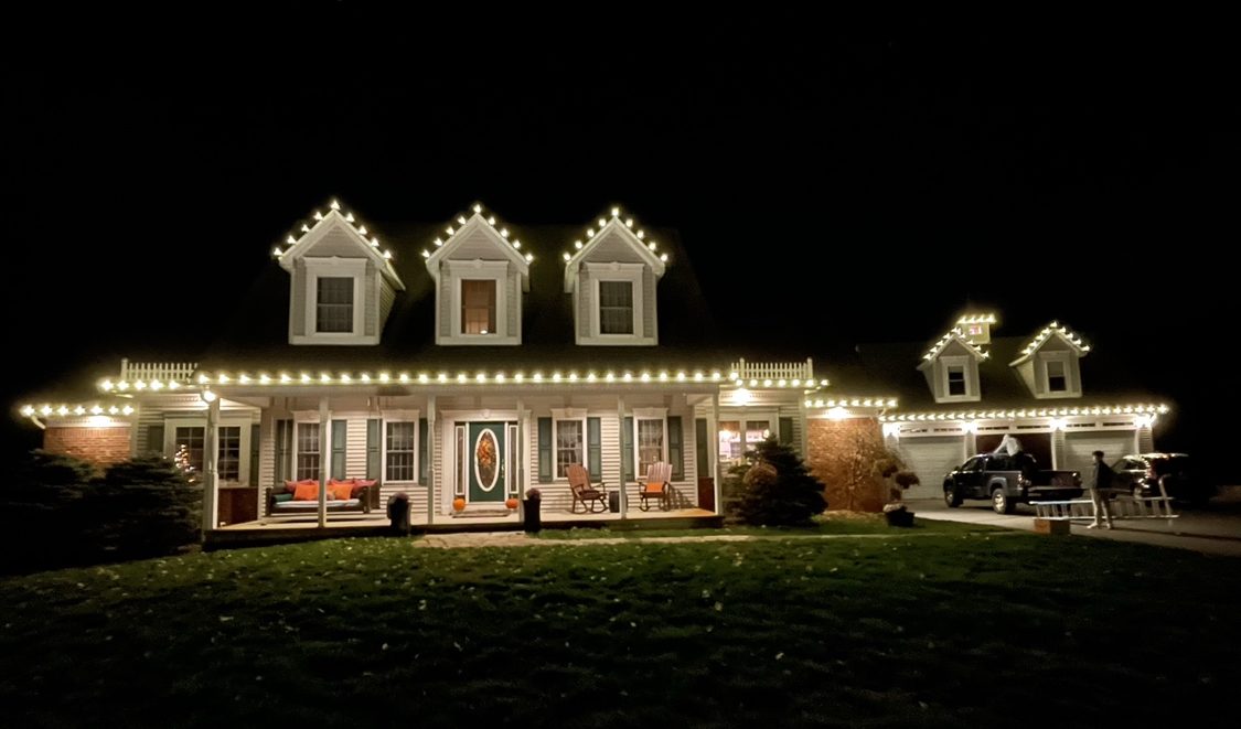 Cape-style home with three dormers and a full front porch outlined in warm white lights