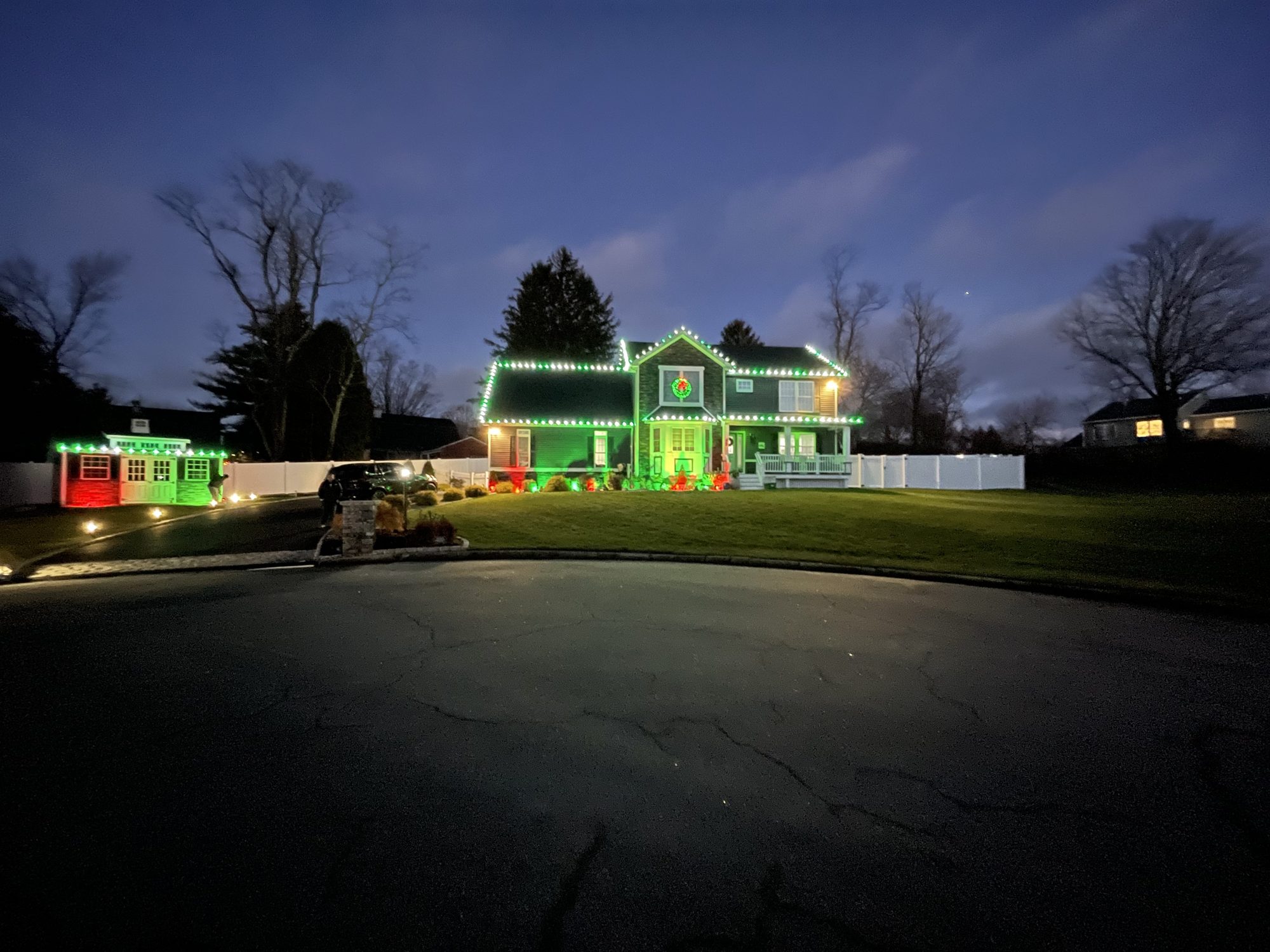 Two-story home and shed outlined in green and red lights at dusk