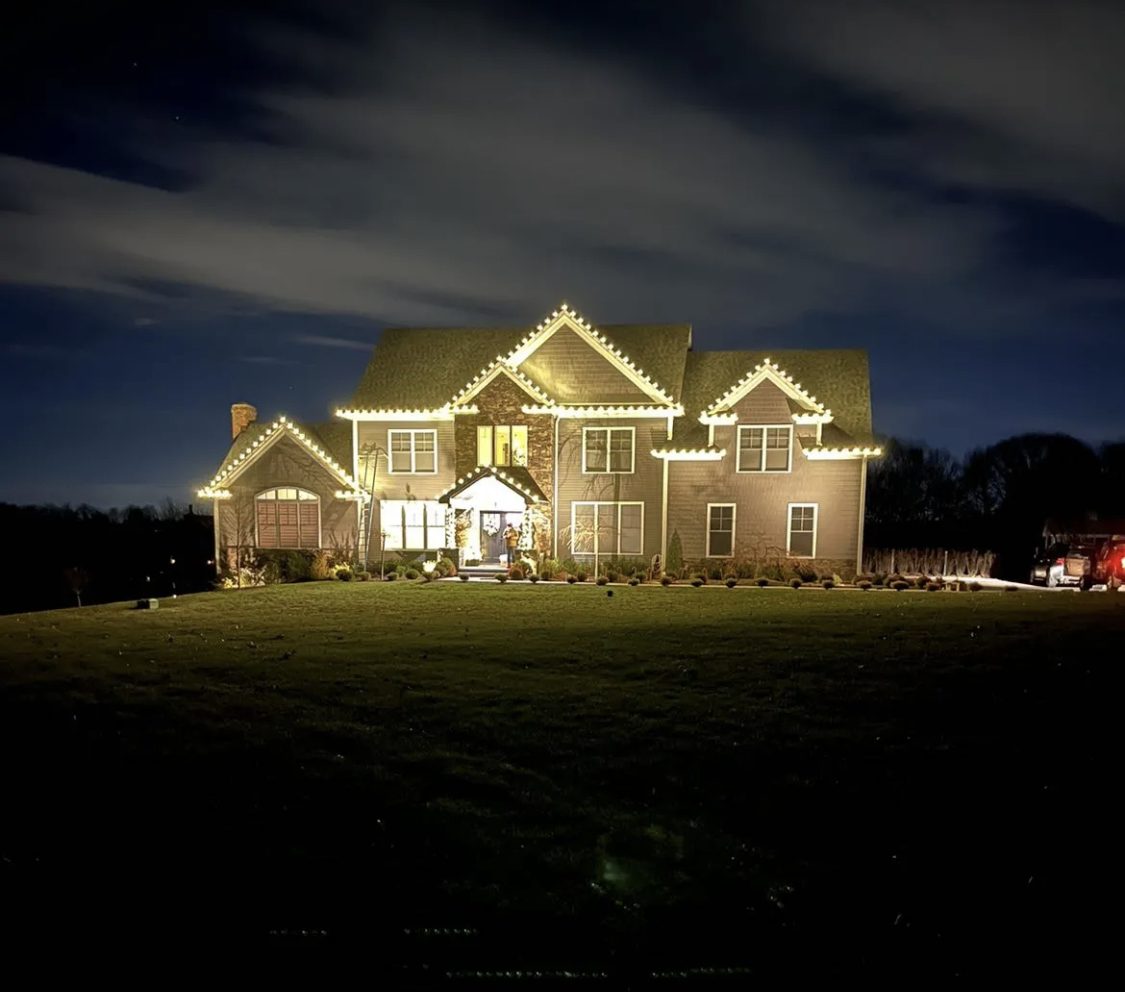 Two-story home on a hill with every peak and gable outlined in warm white roofline lighting